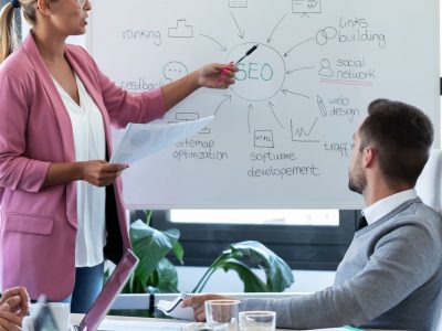 young-businesswoman-pointing-at-white-blackboard-a-PTWUPDS (1)